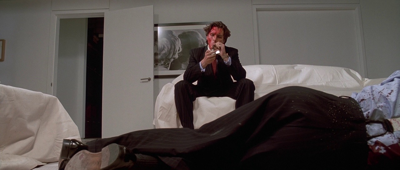 Christian Bale as Patrick Bateman in American Psycho on a couch covered in blood and smoking