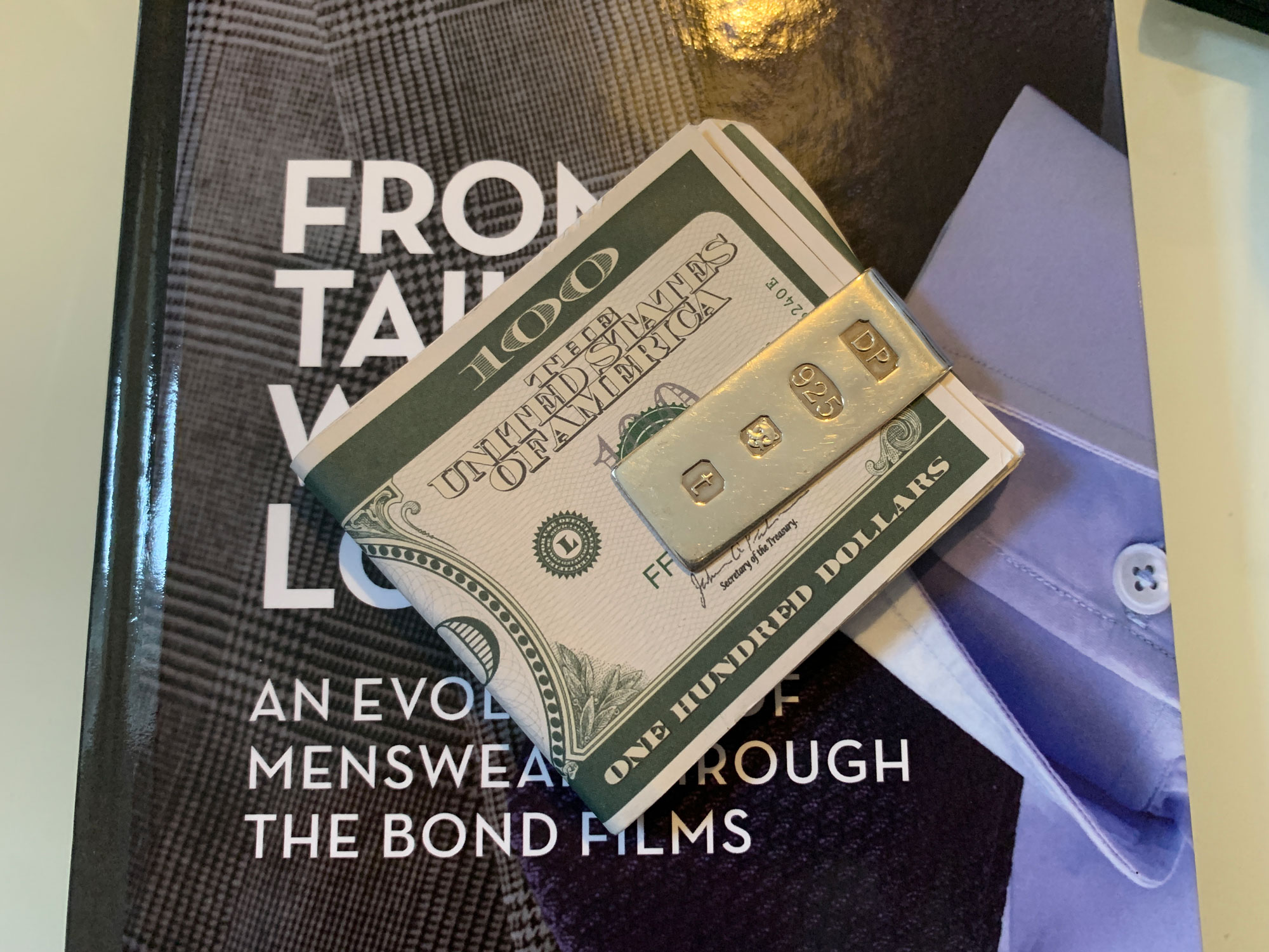 Douglas Pell Money Clip holding dollar bills on top of a book 