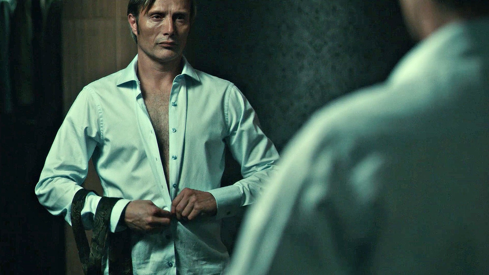 Hannibal doing up his shirt in the mirror